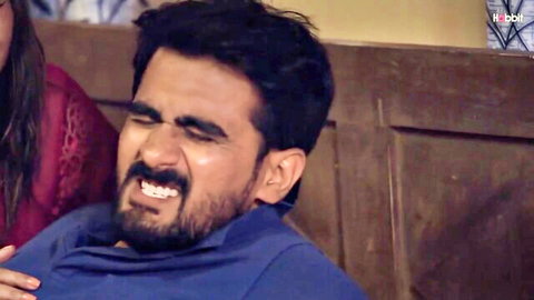 Bearded Indian man grimacing with wide open mouth next to South Asian woman in red top