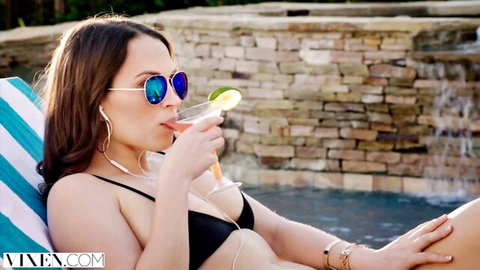 Lily in black string bikini lounging by pool sipping cocktail with lime