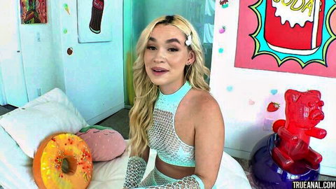Blonde babe in sheer teal mesh lingerie teasing on colorful candy bed with donuts and gummies