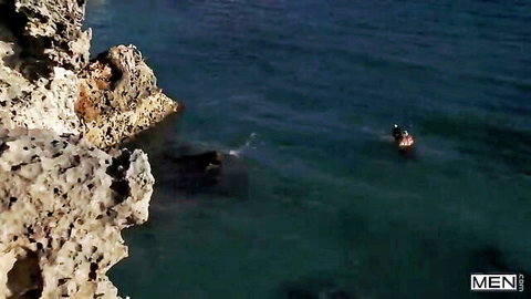 Athletic gay couple kissing passionately in turquoise ocean waves at rocky beach