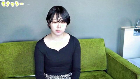 Shy Asian cutie with bangs in black scoop-neck top and skirt sits teasingly on green couch