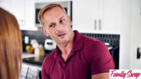 Blonde muscular man in maroon polo confronts redhead woman from behind in kitchen during taboo Family Swap scene