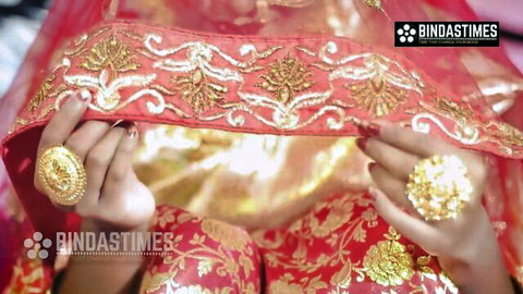 Indian bride lifts red embroidered veil revealing henna hands and gold rings