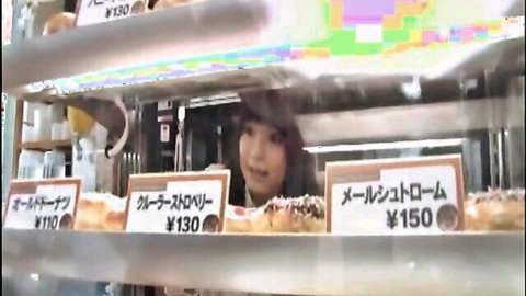Cute Japanese girl smiling behind colorful donut shop counter with pastries