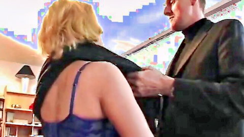 Blonde mature wife in low-back dress embraced by suited man on anniversary