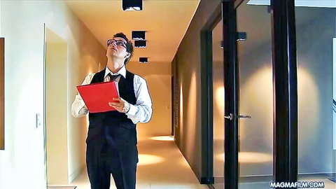 Suited man in vest and tie holding red folder looking up in office hallway.
