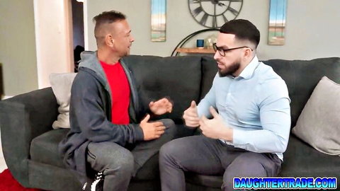 Stepdad in red hoodie gestures animatedly to muscular guy in blue shirt on couch discussing daughter trade