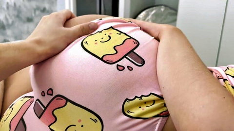 Pregnant babe in cute pink popsicle pajamas, hand gripping her swollen belly intimately