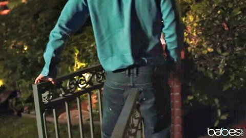 Skinny young brunette in teal shirt leans seductively on garden gate at night teasing her average ass