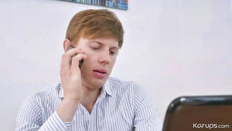 Redhead man in striped shirt talking intensely on phone at office desk