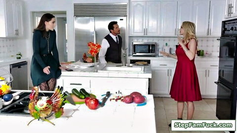 Stepmom in green dress and blonde stepdaughter in red dress with stepson in kitchen threesome