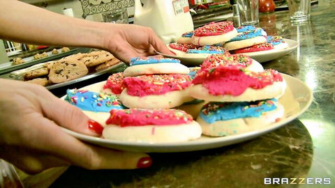 Manicured hands holding plate of pink and blue creamy frosted cookies with sprinkles and milk in kitchen