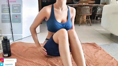 Busty teen in tight blue sports bra and shorts sits knees up spreading legs on webcam