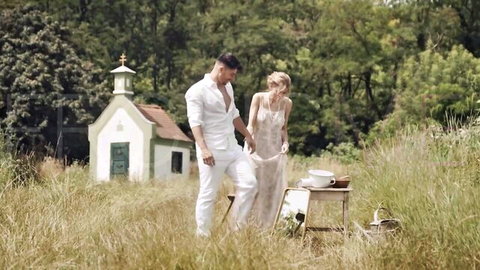 Fanta Sie in white dress holds hands with man in field near chapel