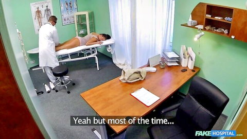 Black doctor in white coat examines busty brunette patient in pink bra on exam table