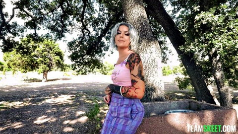 Tattooed skinny white girl with small tits poses sexy in pink TEAM SKEET top and plaid pants outdoors