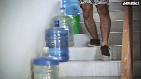 Desi man in patterned shorts climbs stairs with water jugs in amateur setup