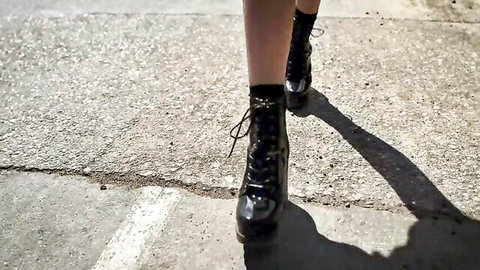 Fair-skinned babe's sexy legs in shiny black lace-up high heel boots strutting on street