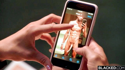 Woman's hands holding pink iPhone displaying muscular black man's nude mirror selfie with huge cock