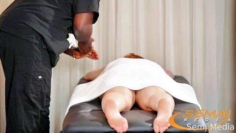 Black masseur rubs redhead babe's bare ass cheeks during intense massage