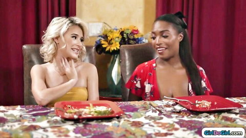 Blonde and ebony women smiling flirtatiously at dinner table in sexy tops