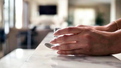 Closeup of feminine hands gripping a shot glass on marble counter in luxurious living room
