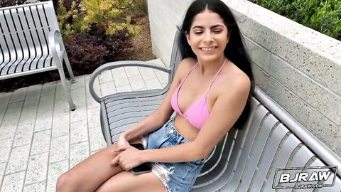 Angel Gostosa in pink bikini top and ripped denim shorts, smiling on outdoor bench