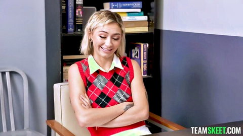 Blonde teen in checkered sweater vest smiles playfully with arms crossed teasing viewers