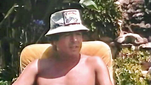 Shirtless mature man in bucket hat lounging outdoors at wild party