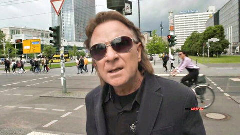 Mature man in sunglasses and suit smirking at busy city intersection with traffic