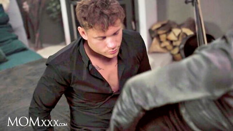 Handsome young stud in open black shirt gazing down intently with exposed chest tattoos