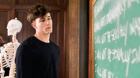Young curly-haired student in black shirt stands by skeleton in classroom, teacher roleplay tease