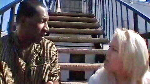Black man and blonde white woman close on sunny outdoor stairs, teasing interracial heat