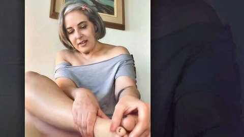 Gray-haired MILF in off-shoulder top smiles as hand caresses her bare foot toes