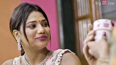 Seductive Indian woman in pink saree holding cup, smiling at camera