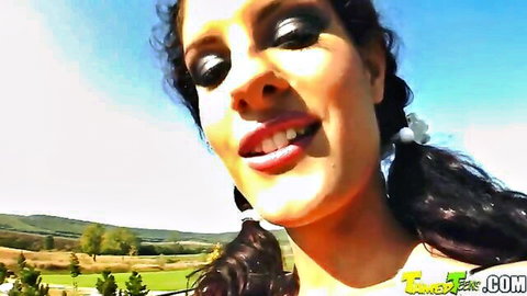 Brunette with curly pigtails smiles with open mouth outdoors teasing blowjob