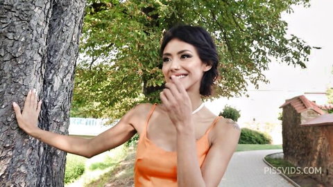 Veronica Leal smiles seductively leaning on tree in orange dress outdoors