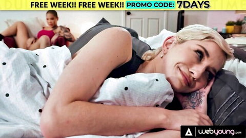 Smiling blonde teen with medium tits lies on bed beside brunette in lesbian tease