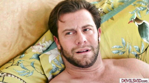 Shirtless bearded brunette hunk lying on floral bed sheets with surprised aroused expression