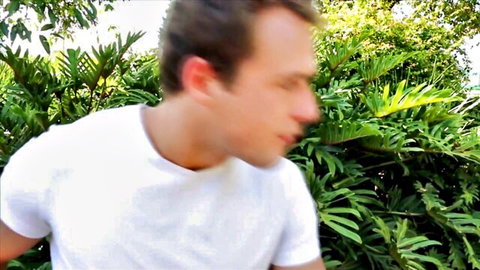 Athletic man sprinting shirtless-like in tight white tee through lush tropical jungle revealing toned arms
