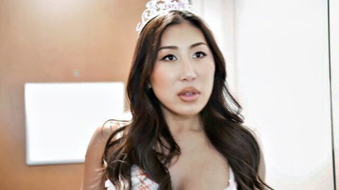 Young Asian beauty with long brunette hair and tiara teasing deep cleavage in sparkly top