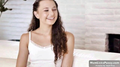 Smiling curly-haired brunette teen in white lace tank top on couch