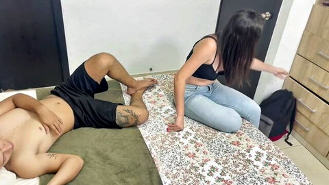 Brunette in black bra reaches toward shirtless tattooed guy lying on mat
