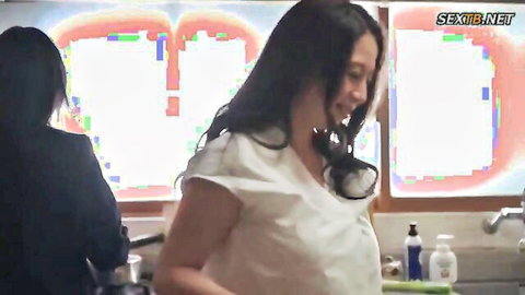Asian MILF in white top smiles with daughter watching in kitchen scene