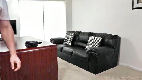 Bedroom casting couch setup with black leather sofa, checkered pillows, wooden desk and controller