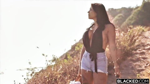 Curvy olive brunette with massive tits in deep V black top and tiny denim shorts posing on sunny cliffside