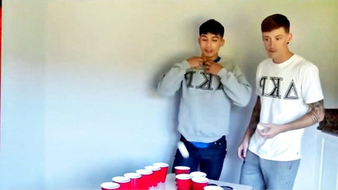 Two frat guys in casual wear tossing ping pong ball at red cups before raw threesome