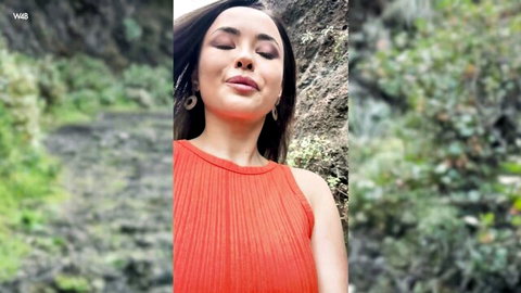 Sexy Asian model in tight orange top poses sensually outdoors among rocks and greenery
