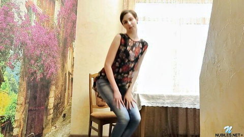 Brunette teen with short hair posing sensually in floral tank top and tight jeans by window