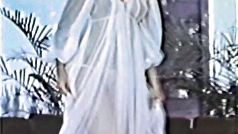 Vintage softcore model in flowing white gown, ethereal pose in dim light
